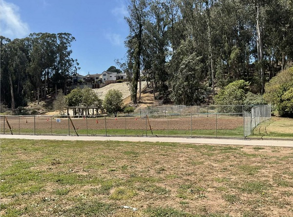 Photo shows dog park in Pine Lake meadow, surrounded by fencing, with soil preparted for new sod