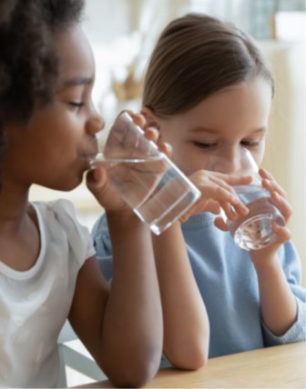 photo of two girls drinking water out of clear glasses