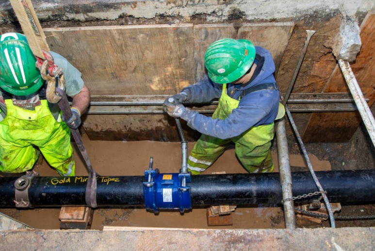 photo of two workmen in a pit making a water main connection