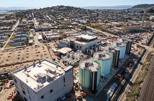 Aerial view of an industrial facility with large cylindrical tanks and surrounding buildings near a residential area.