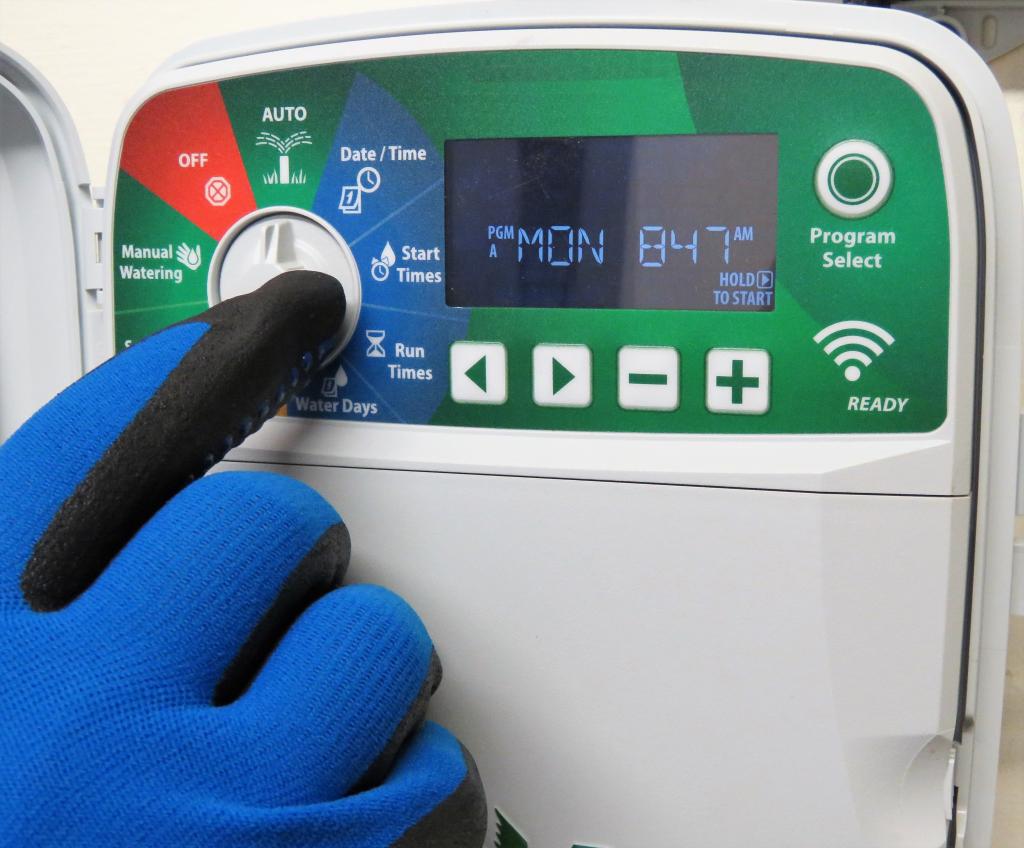 Person with gardening glove on setting the timer on their irrigation controller. 