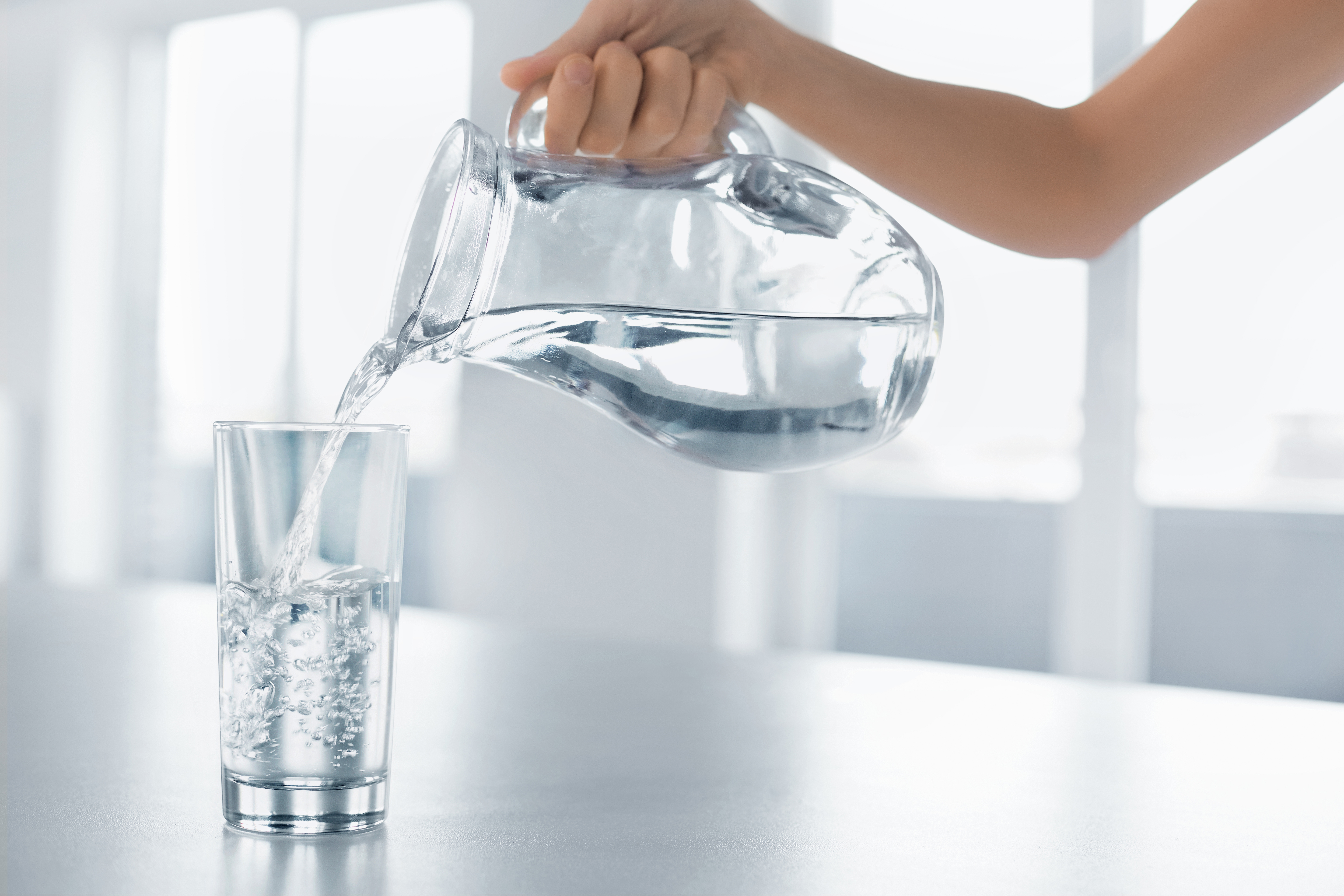 Person pouring water into a glass from a clear water pitcher.