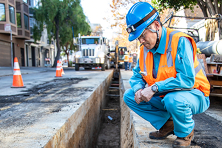 Construction worker inspecting underground pipe in a trench