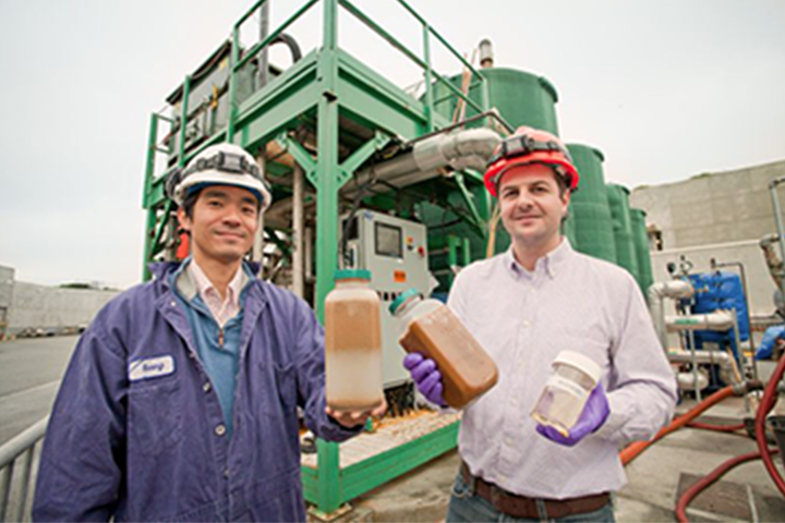 two men holding jars of waste grease