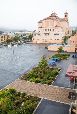 Lushly planted rain garden with a tiled walkway through it, amid large paved basketball court area with large salmon-colored church behind it