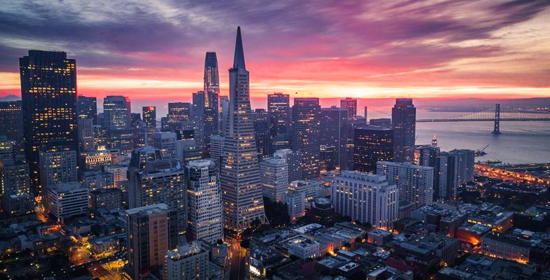 Cảnh quan thành phố San Francisco lúc hoàng hôn với tòa nhà Transamerica Pyramid và cầu Bay Bridge được chiếu sáng rực rỡ trên nền trời đầy màu sắc.