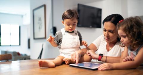 Mother and two children sit at a table looking at a tablet.