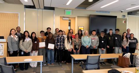 Group of diverse students and SFPUC staff standing in a room, some holding certificates, smiling at the camera.