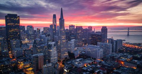 San Francisco skyline at sunset with the Transamerica Pyramid and Bay Bridge illuminated against a colorful sky.