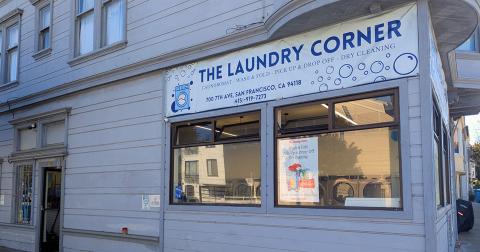 Exterior view of The Laundry Corner, a laundromat with a white facade and large windows on a street corner.