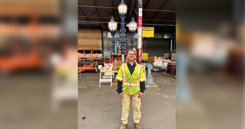 Man in a reflective safety vest standing in a warehouse with a decorative street lamp behind him.