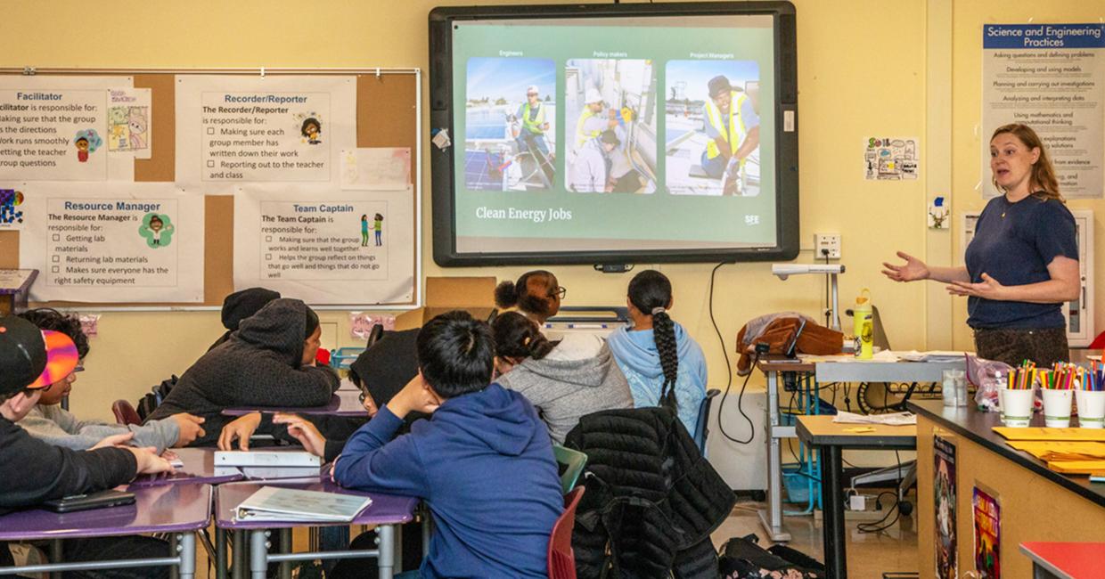 Person explaining clean energy jobs to SFUSD students in a classroom setting with educational posters on the walls.