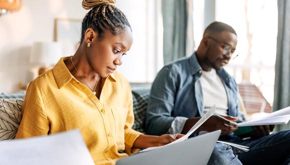 Woman in a yellow short and a man with glasses, both reading.