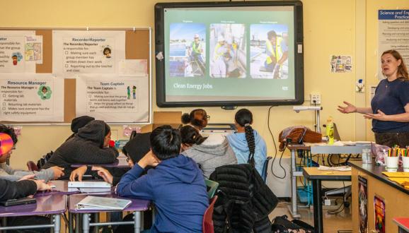 Person explaining clean energy jobs to SFUSD students in a classroom setting with educational posters on the walls.
