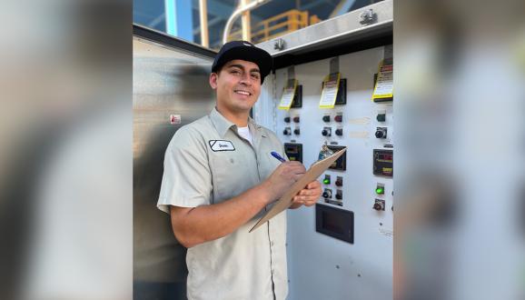 Davin Clark, Stationary Engineer at the SFPUC, standing in front of a machine with a notepad and pen.