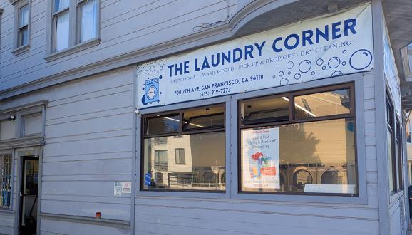 Exterior view of The Laundry Corner, a laundromat with a white facade and large windows on a street corner.