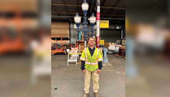 Man in a reflective safety vest standing in a warehouse with a decorative street lamp behind him.
