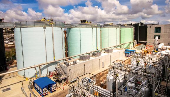 Large industrial storage tanks at a chemical plant under a partly cloudy sky.