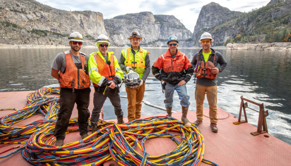 A team of commercial divers wearing safety vets and hard hats standing at a resrvoir.